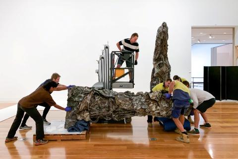 An installation team moves a large sculpture in a bright gallery space
