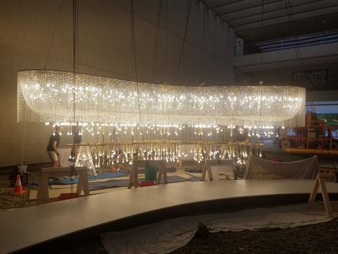 A huge chandelier-style work, lit up, undergoing conservation work in QAG's Watermall space.