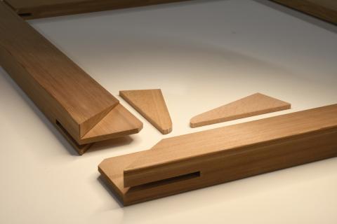 Timber artwork stretchers mid-construction: two long pieces of timber, and two small triangle-shaped pieces on a white table