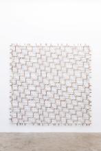 An acrylic work that appears to be woven together; displayed on a white wall it looks like a lace net or quilt.