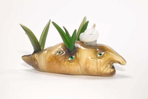 A glass sculpture of a hybrid creature: a slug that looks like a potato, with multiple eyes, sprouting greens and a sour-cream hat.