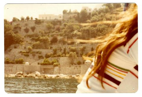 A vintage colour photograph in which a person's back and hair are visible against a rocky landscape and glimpse of river.