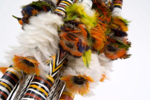 A detail view of orange, green, black and white feathers that form part of a Morning Star pole design