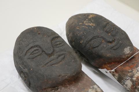 A photograph of the heads of two carved, figurative wooden sculptures