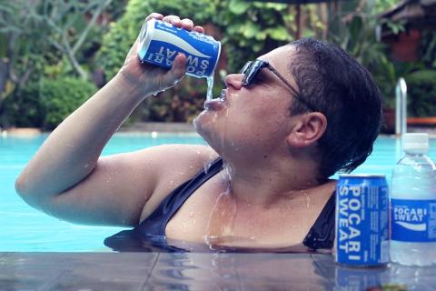A photograph of a person in a swimming pool, drinking from blue cans of Pocari Sweat
