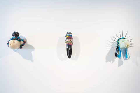 Three peculiar sculptures made from plastic bottles and other 'found' components installed on a white gallery wall