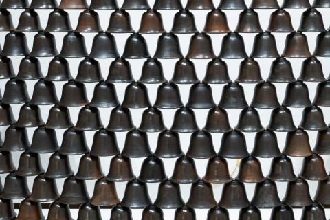 A detail view of a sculpture made from rows of ceramic bells, stacked so as to form a wall