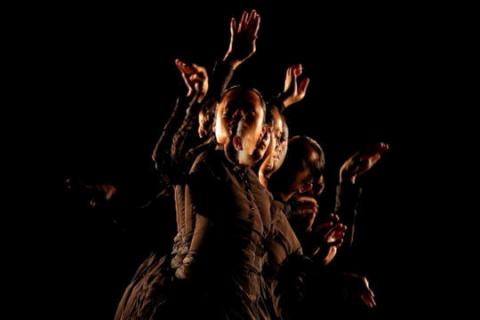 In this still from a portrait-oriented video work, a Sāmoan woman dressed in late nineteenth-century, western-style clothing is captured mid-dance. Illuminated against a dark background, a transparent motion trail of the figure's previous movements is also visible.