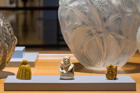 A view of miniature Netsuke sculptures installed in a gallery vitrine, with a large glass vase in the background.