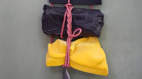 An installation view of a sculpture that appears to be made of a rubber band holding together black and yellow chunks of foam.