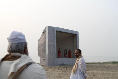 A photograph of two men in the foreground of a field; in the background is a giant empty CRT TV set, with several people standing inside as if 'on' the television.