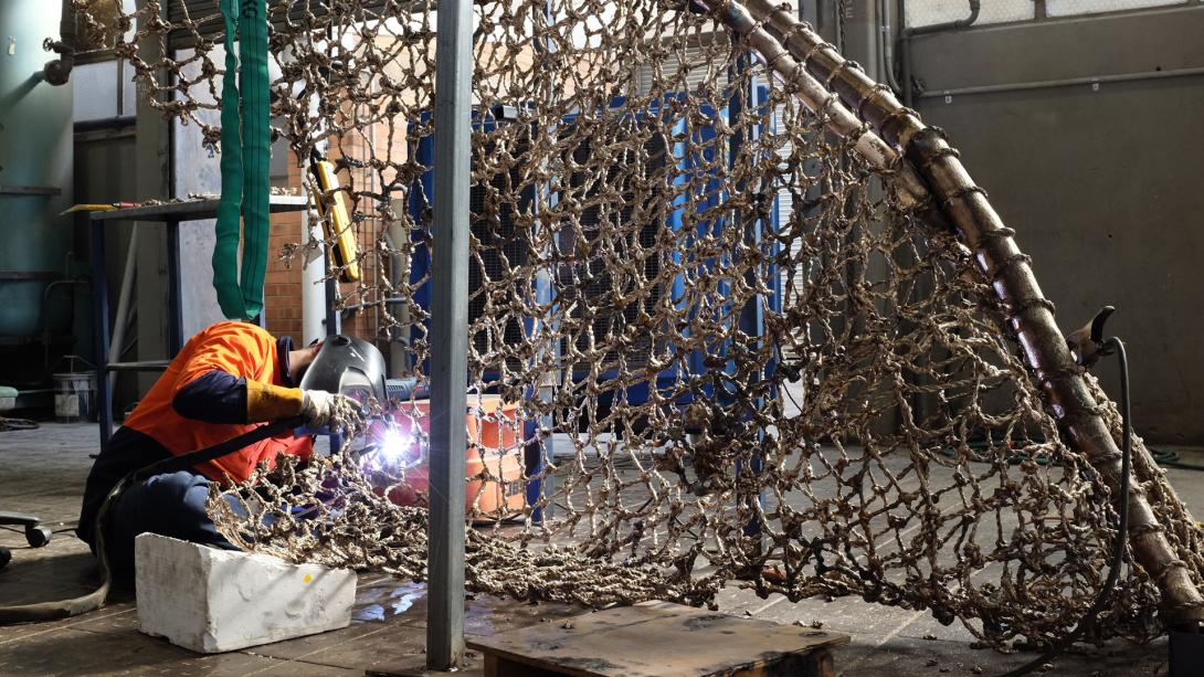 A craftsman wearing protective gear works on a fishing net cast in bronze.