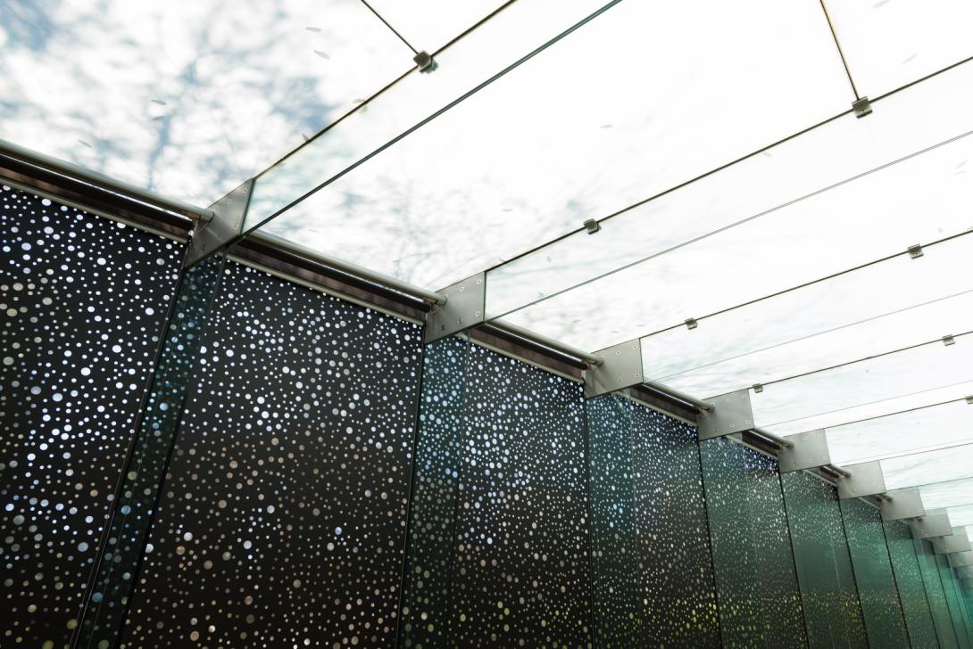 An installation view of a black vinyl window treatment covering a gallery window, with clouds above visible though the glass ceiling.
