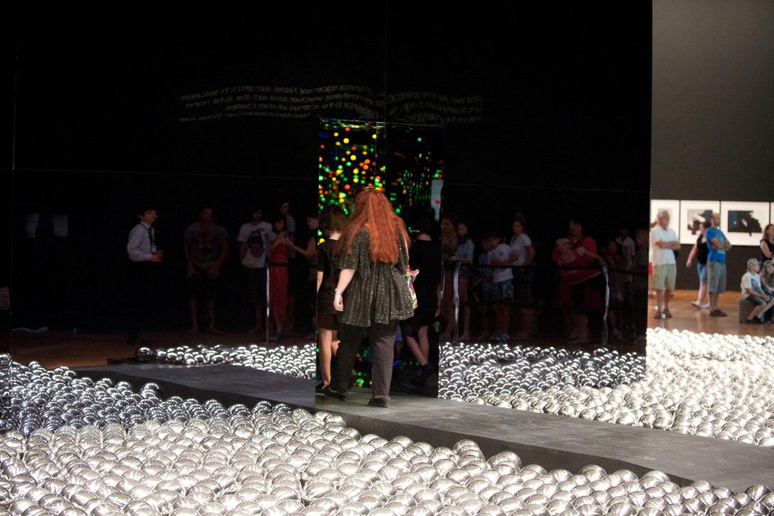 A view of a gallery space in which visitors can be seen walking into an installation