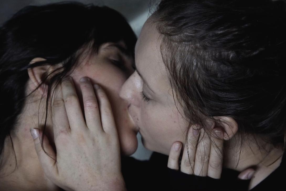 A photograph of two women kissing, with their hands tenderly placed on one another's faces.