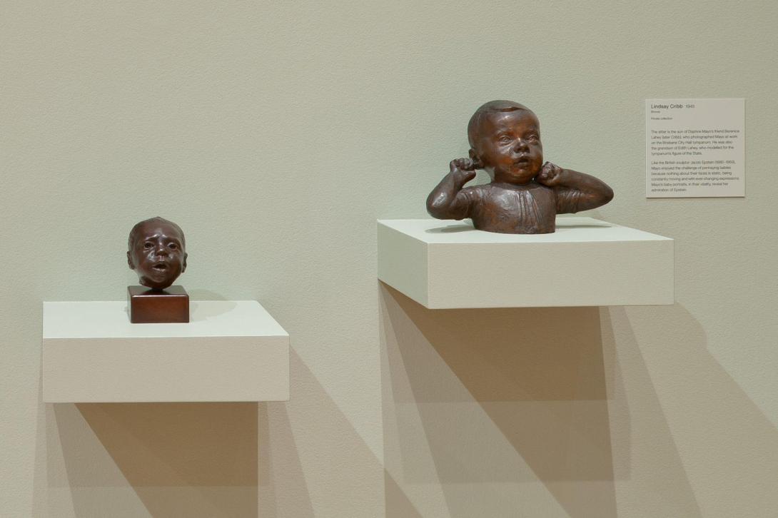 Bronze statues installed on plinths in a gallery space with sage green walls