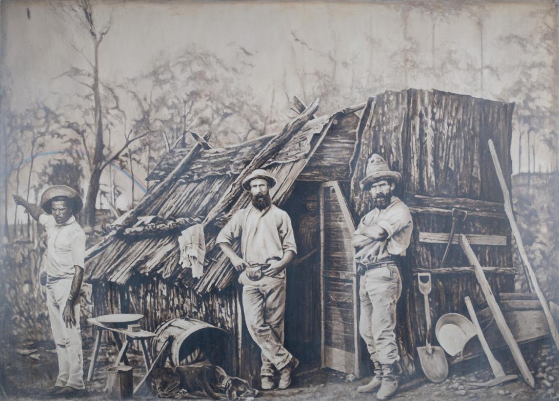 A sepia-toned image of two male colonial settlers standing either side of the open door of a bark slab hut, accompanied by a First Nations Australian man, possibly a tracker, who gestures to a faint rainbow in the distance to the left of the image. A First Nations Australian woman can be seen in the doorway, obscured by the shadowy interior.