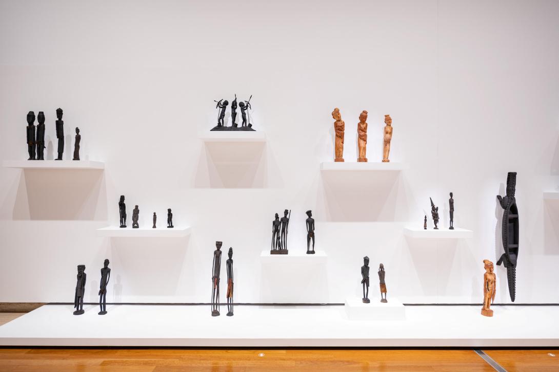 Numerous small wooden sculptures installed in a gallery space.