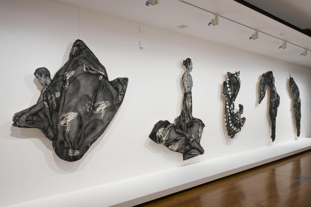 Figures rendered as realistic black and white drawings, displayed on a white gallery wall