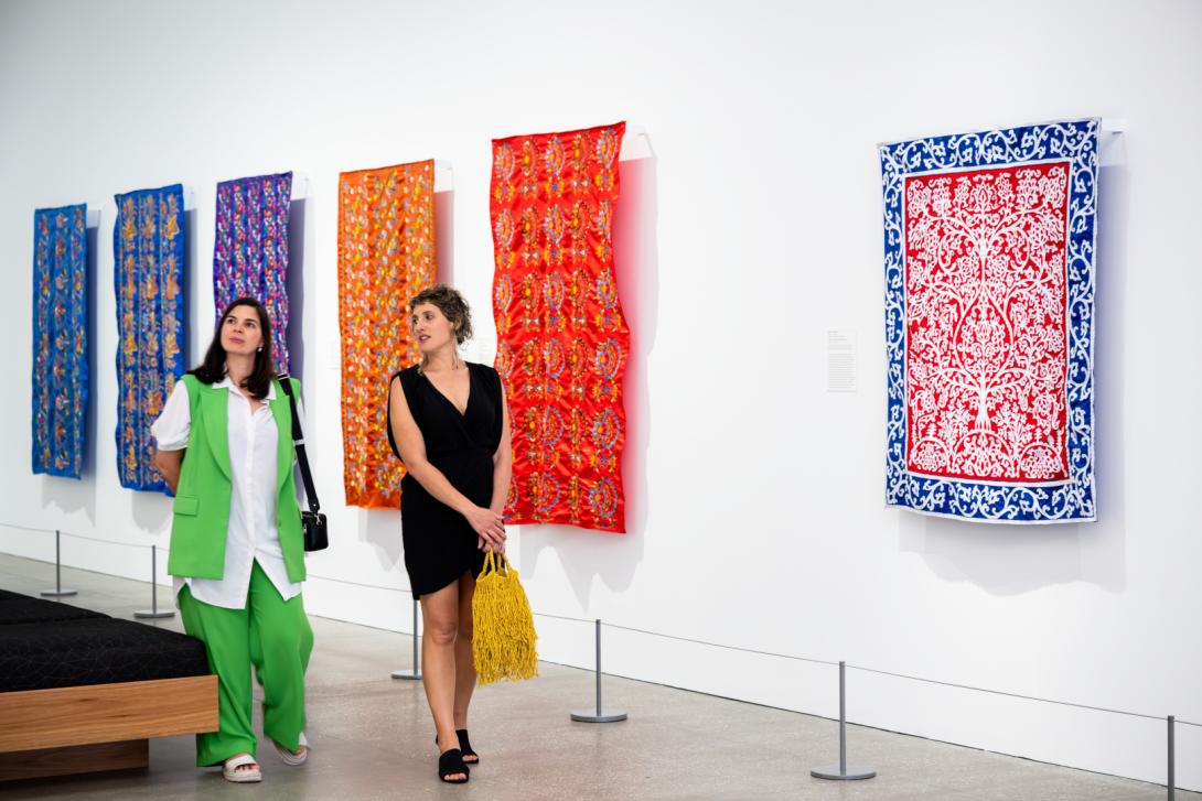 Brightly coloured textile works installed in a bright gallery space, with visitors walking by