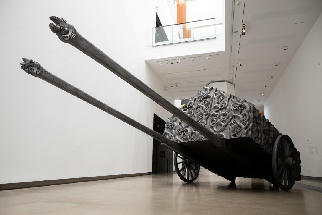 A large sculptural work that evokes a tank or large, laden wagon, installed in a bright gallery space.