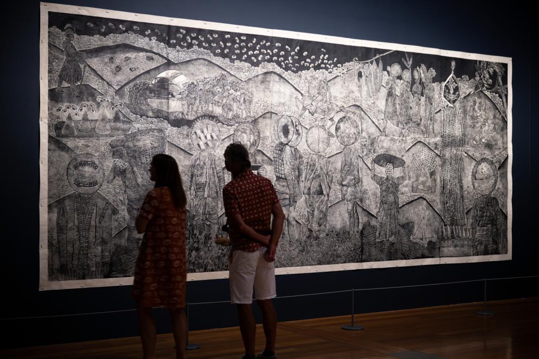An installation view of a large woodcut print, with visitors looking on