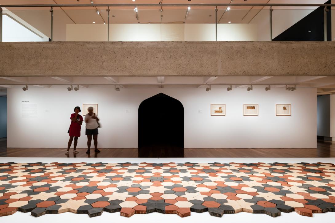 A view of an installation of ceramic tiles laid out in a tessellated pattern on a wide plinth in a gallery space