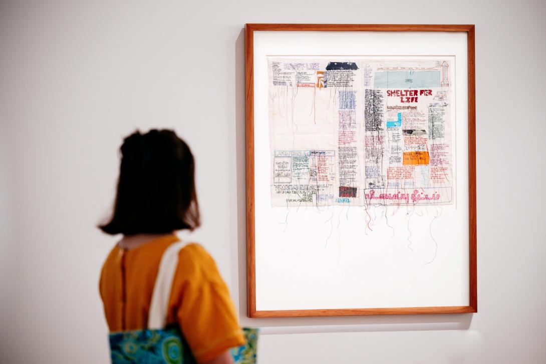 A visitor views a textile work, with embroidered detail and the words 'Shelter For Life'