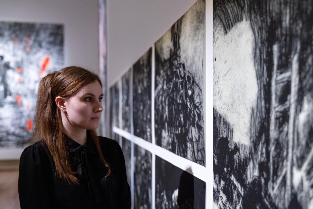 A person wearing black looks upon black-and-white prints installed on a gallery wall