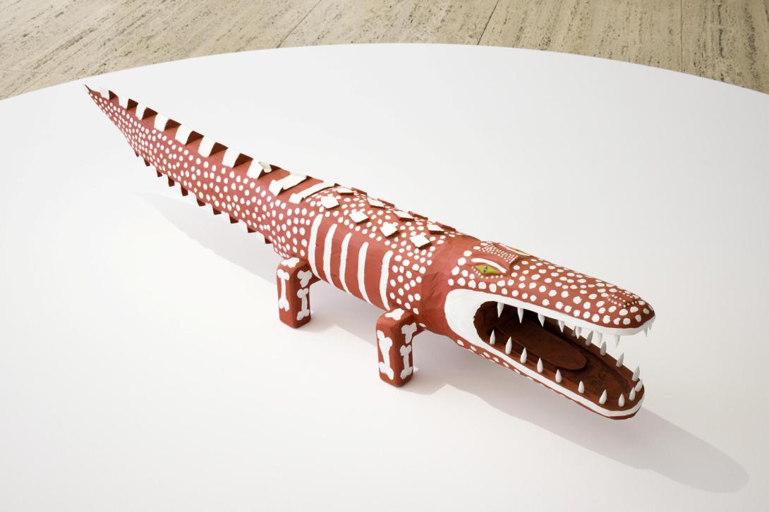 An installation view of a sculpture of a saltwater crocodile, painted with ochre-red designs