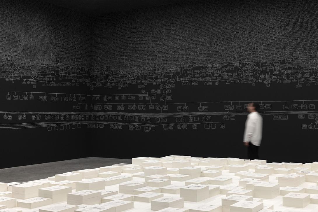 A visitor explores a room-scale installation work, with chalk designs on black gallery walls and, in the foreground, a white sculptural work