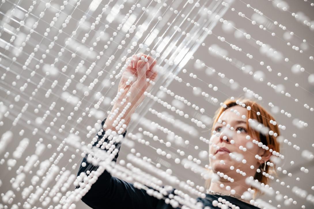 A photograph of a gallery employee installing a delicate work made from thread and styrofoam.