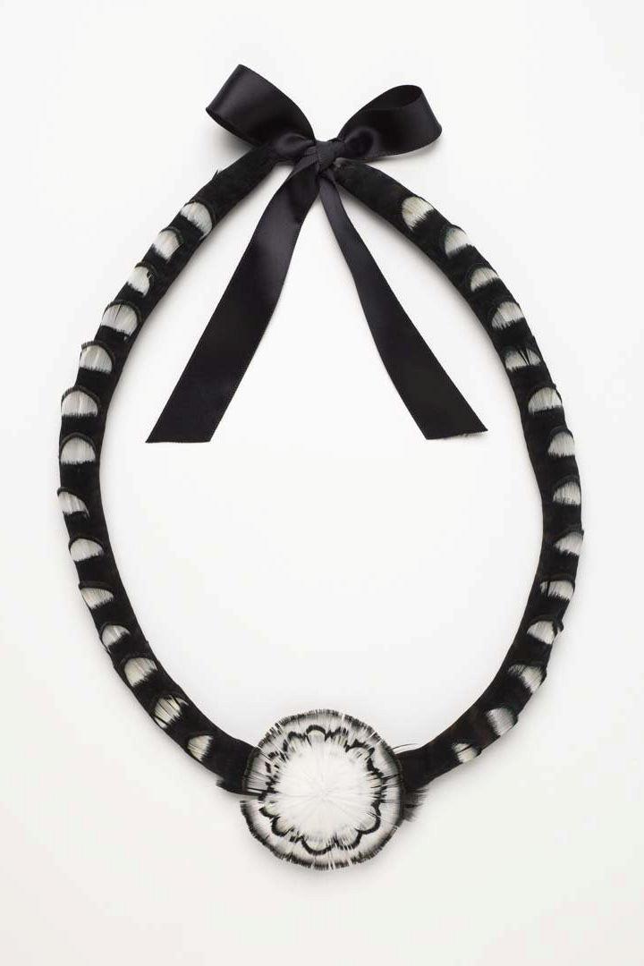 A necklace made with black and white feathers and ribbon, photographed on a white background