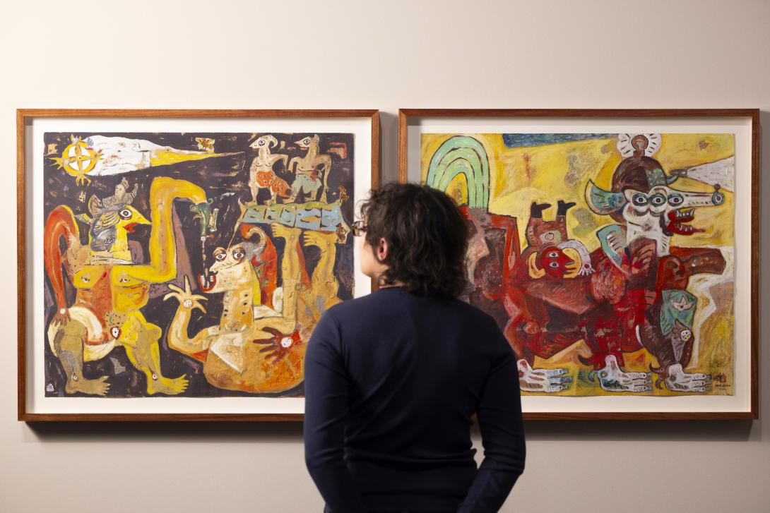 A gallery visitor views two brightly coloured paintings by Indonesian artist Heri Dono, installed on a cream-coloured gallery wall