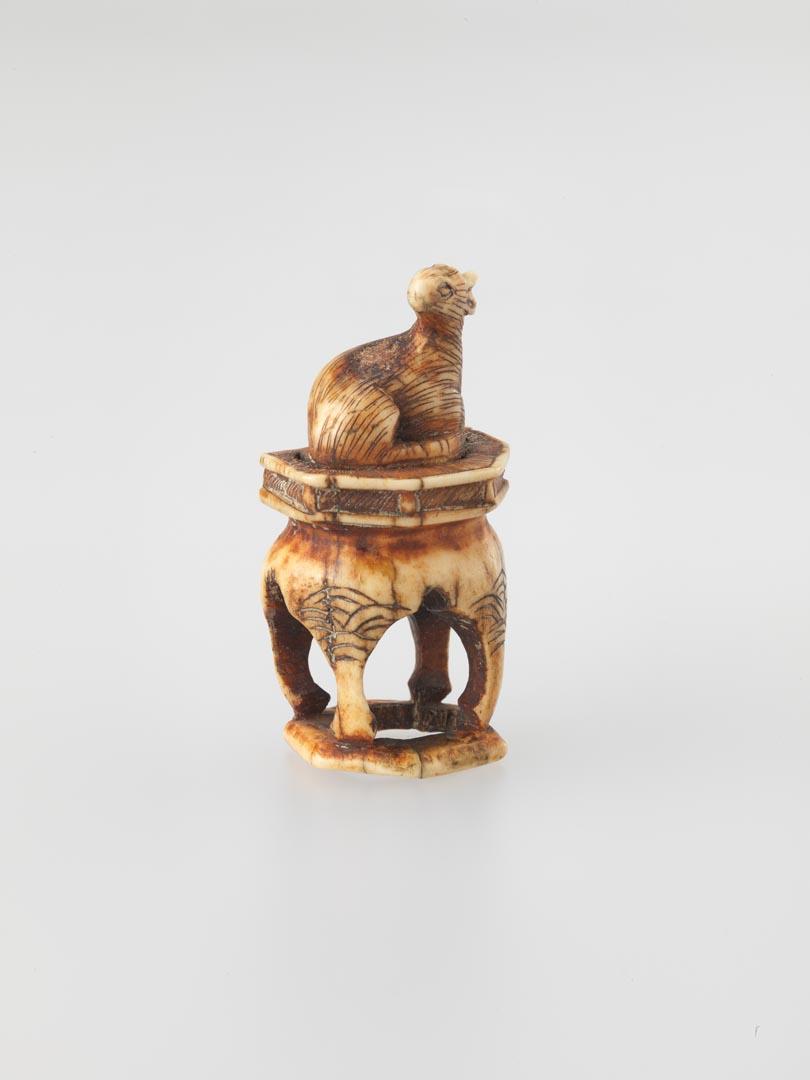 Artwork Netsuke:  (deer seated on a table) this artwork made of Carved horn, created in 1800-01-01