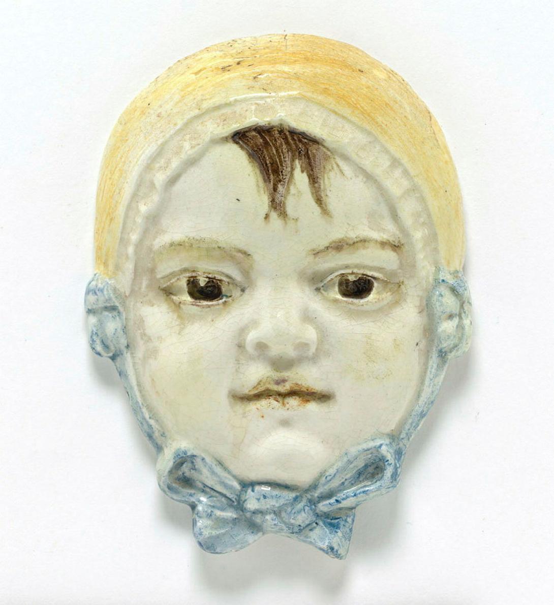 Artwork Plaque: Baby girl in bonnet and bow this artwork made of Earthenware, white clay modelled with details in brown, yellow and blue, created in 1936-01-01