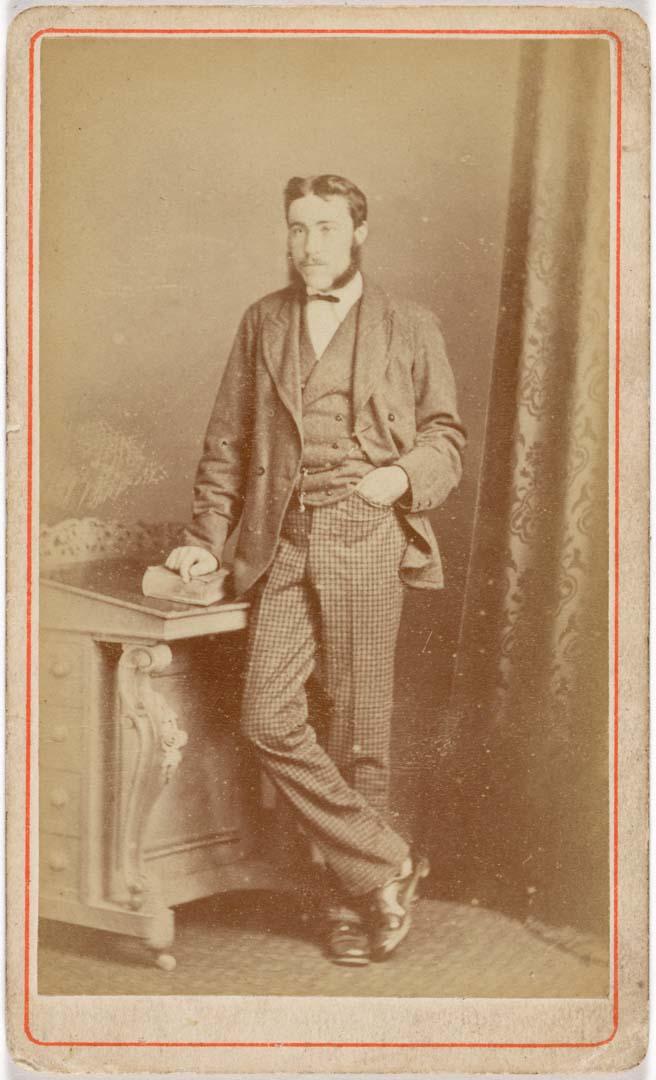 Artwork (Young man standing beside desk) this artwork made of Albumen photograph on paper mounted on card, created in 1880-01-01