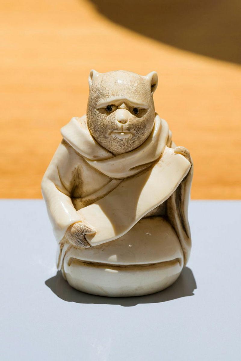 Artwork Netsuke: (tanuki priest standing on mogyoku drum) this artwork made of Carved ivory, created in 1800-01-01