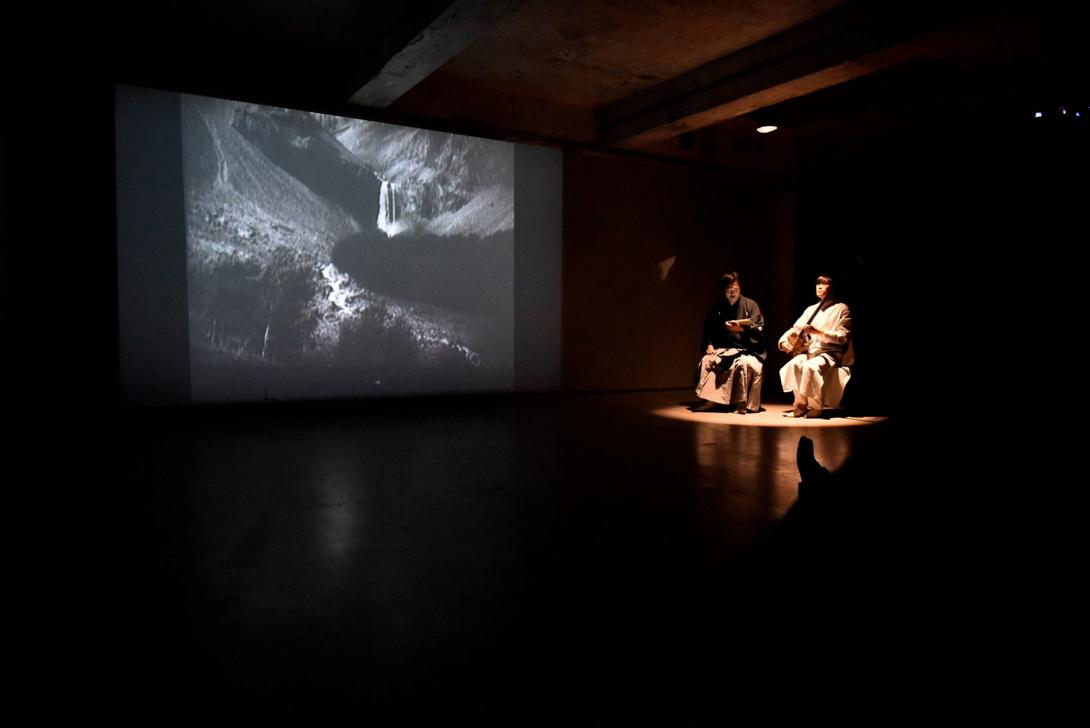 A photo of two men seated under a spotlight in front of a cinema screen