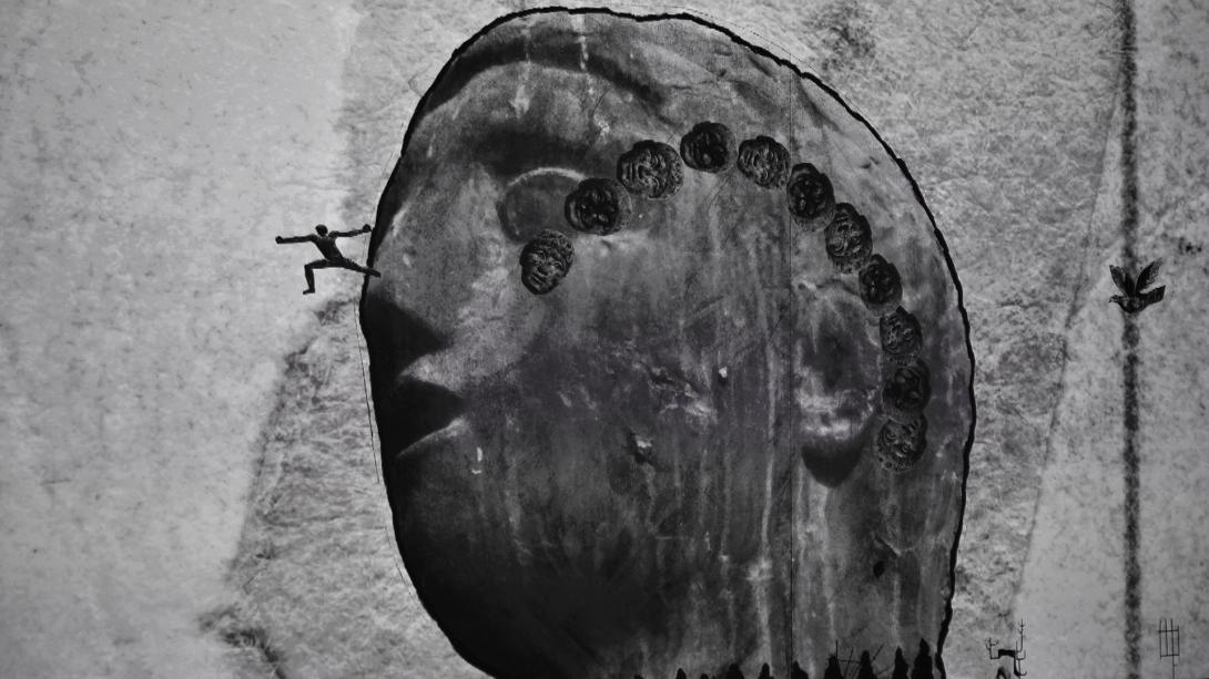 A video still of a huge carved stone head, which appears to have a person climbing up the side.