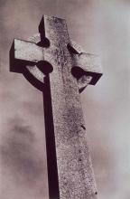 A black and white photograph of a Celtic cross in a graveyard