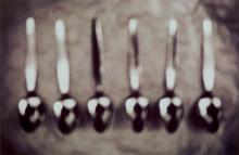 A black and white photograph of six teaspoons laid out in a row