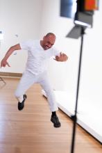 A man dressed in white leaps in the air in a gallery space.