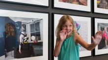 An installation view in APT Kids, with a child holding a superhero pose before a gallery wall hung with photographs.