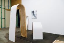 An installation view of abstract sculptures made of plywood, which appear to lean and bend on the floor and against walls, in a gallery space.