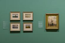 An installation view of five oil paintings installed on a sage-green wall.
