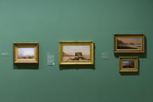 An installation view of four oil paintings in gold frames installed on a sage-green wall.