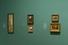 An installation view of five oil paintings installed on a sage-green wall.