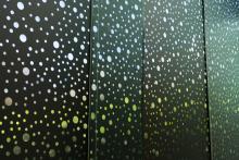 An installation view of a black, perforated vinyl window treatment covering a floor-to-ceiling gallery window.