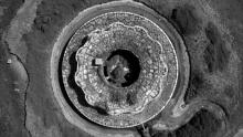 A black-and-white aerial photograph looking down on a circular mine-type structure set in the earth.